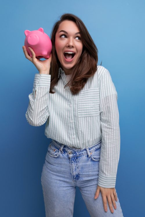 joyful brunette young business woman in a shirt keeps her savings in a piggy bank.